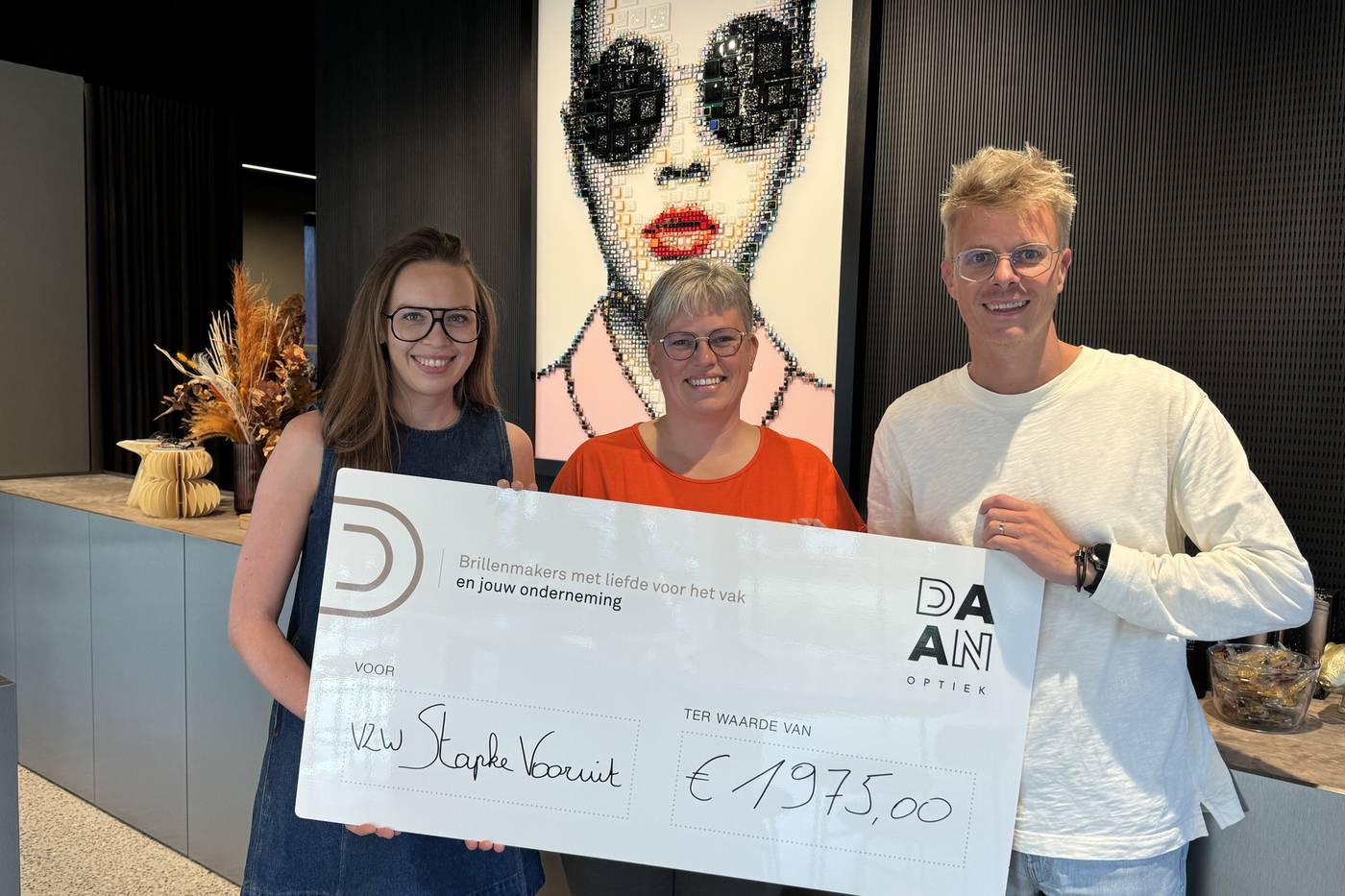 Overhandiging van een cheque van &euro;1.975 aan vzw Stapke Vooruit in Daan Optiek; Daan rechts, twee vrouwen links, grote cheque in het midden.